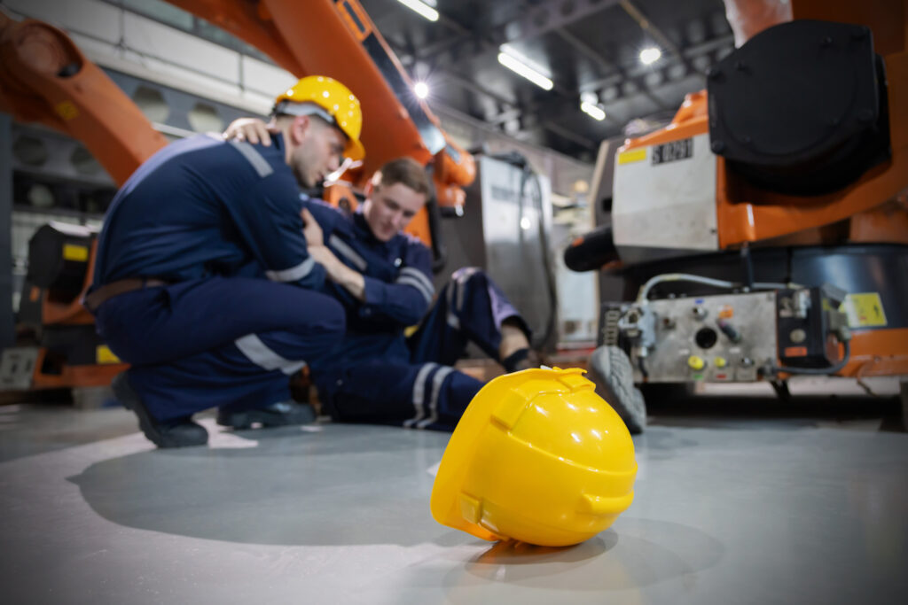 로보틱 암(로봇 팔) 공장에서 백인 노동자들이 다친 동료를 돕고 있다