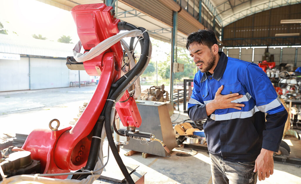 자동차 부품 제조 현장에서 산업용 로봇 암 근처에서 작업 중인 작업자의 모습